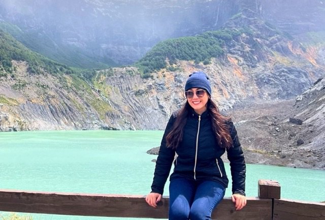 Gabriela sentada na cerca com o cerro tronador e vestisqueiro negro no fundo em bariloche no verao